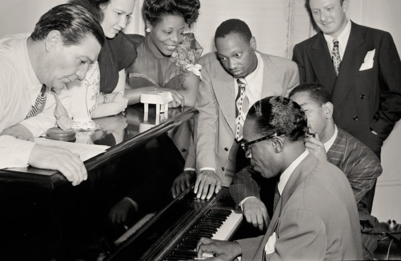 En la imagen, la compositora Mary Lou Williams (tercera desde la izquierda), el compositor Tadd Dameron (cuarto), junto a Hank Jones (al piano) y Dizzy Gillespie, en 1947. US Library of Congress. Colección William Gottlieb. Dominio público.